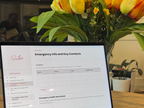 A laptop screen displaying a digital document template titled 'Emergency Info and Key Contacts' in a home office setting, with a large vase of yellow and orange tulips in the foreground.
