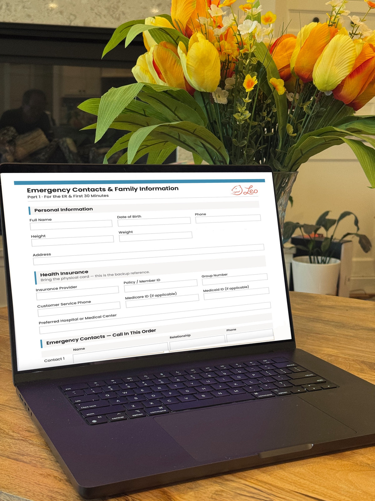 A black laptop on a wooden table displaying a digital form template titled 'Emergency Contacts & Family Information' by the brand 'Delfino'. The background features a large, vibrant bouquet of yellow and orange tulips in a vase, with a blurred indoor setting behind them.